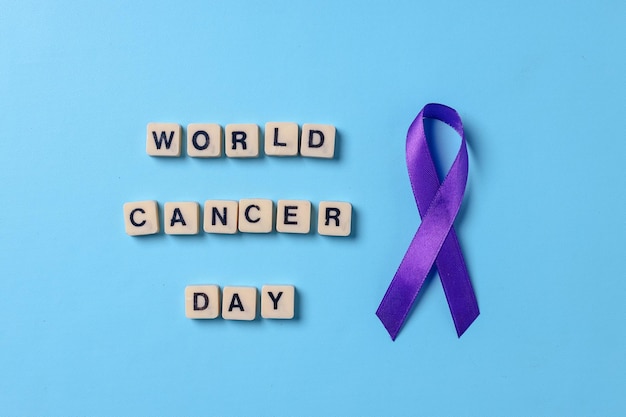 Cinta morada o violeta con el día mundial del cáncer en un cubo alfabético sobre fondo azul.