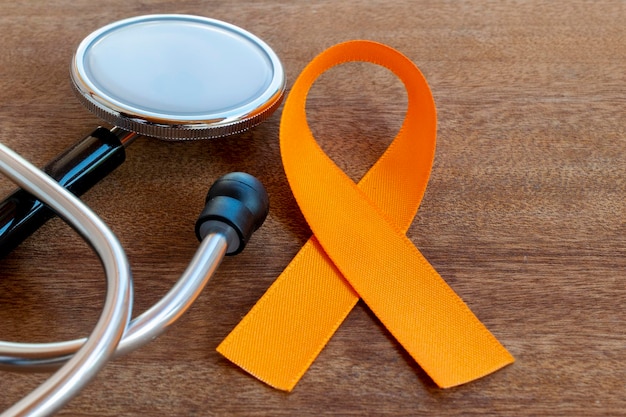 Cinta naranja y estetoscopio en campaña de mesa de madera para prevenir el cáncer de piel melanoma