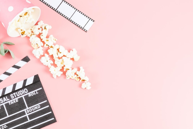 Cinta de película de claqueta de cine y vaso de papel con palomitas de maíz espolvoreadas en un rosa