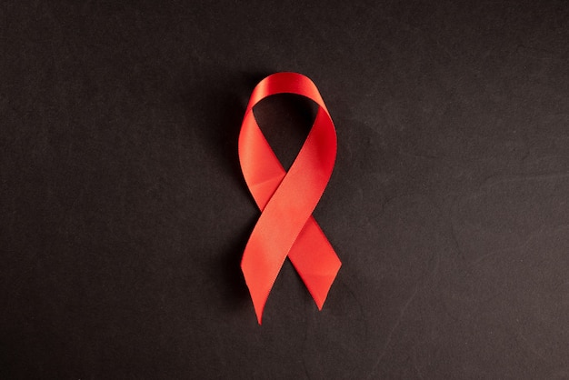 Cinta roja VIH, SIDA sobre fondo negro, conciencia, signo médico. Copie el espacio.