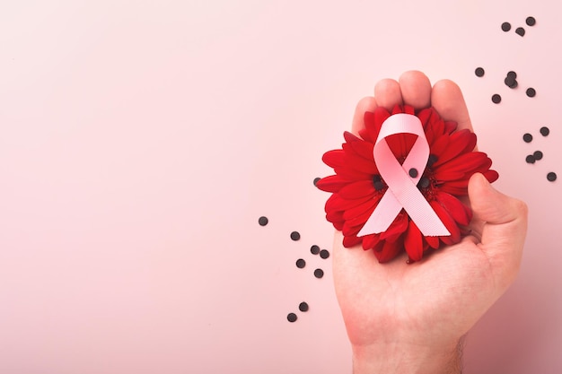 Cinta rosa de concientización sobre el cáncer de mama Manos sosteniendo gerbera roja y cinta rosa en los fondos Concienciación sobre el cáncer de mama y Día mundial del cáncer de octubre Día rosa Vista superior Maqueta