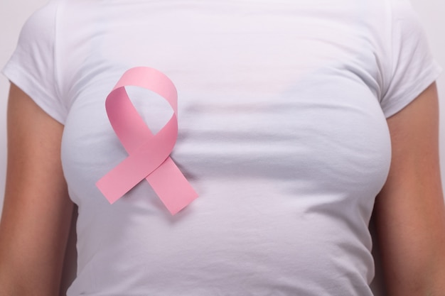 Cinta rosa en el pecho femenino, símbolo de lucha contra el cáncer de mama.