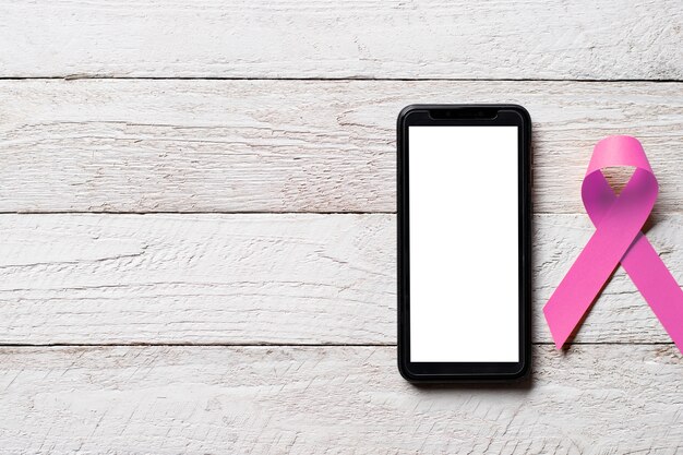 Cinta rosada para el día de la campaña contra el cáncer de mama y el teléfono inteligente con pantalla en blanco.