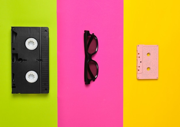 Cinta de video, gafas de sol, cinta de audio en una superficie de papel multicolor. Tendencia minimalista, plano, vista superior.