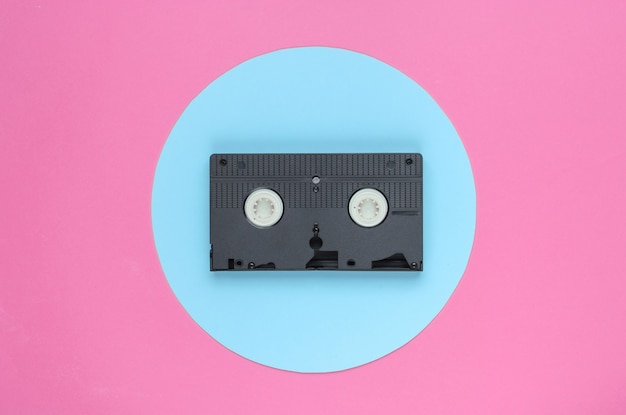 Cinta de video sobre fondo rosa con círculo azul pastel. Concepto retro minimalista. Años 80. Vista superior