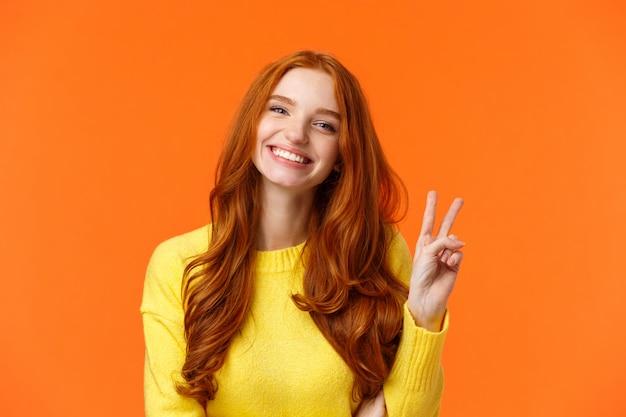 Cintura para arriba alegre mujer hermosa pelirroja con el pelo rojo largo y rizado, mostrando el signo de la paz