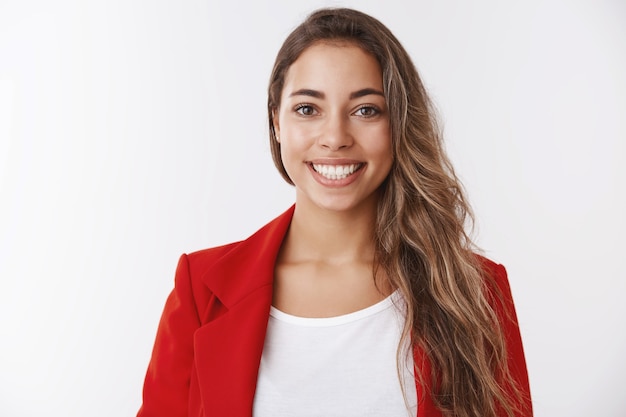 Cintura para arriba exitosa mujer europea atractiva afortunada vistiendo chaqueta roja sonriendo dientes blancos manteniéndose positivo, sintiéndose optimista obteniendo promoción logrando objetivo, recibiendo cumplidos, luciendo satisfecho