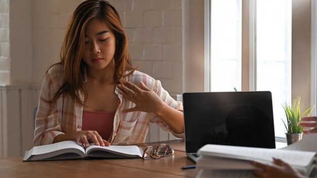 Cintura para arriba hermosa mujer en camisa a rayas leyendo un libro escolar mientras está sentado