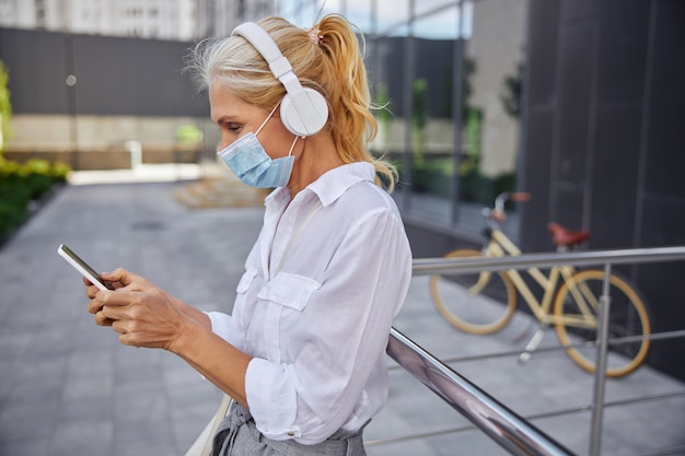 Cintura para arriba retrato de dama de negocios en camisa blanca con máscara protectora mientras escucha música en los auriculares