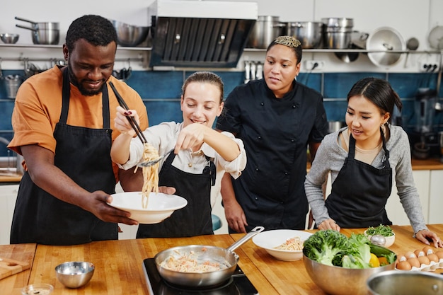 Cintura para arriba retrato de diverso grupo de personas cocinando juntos durante el taller en la cocina profesional