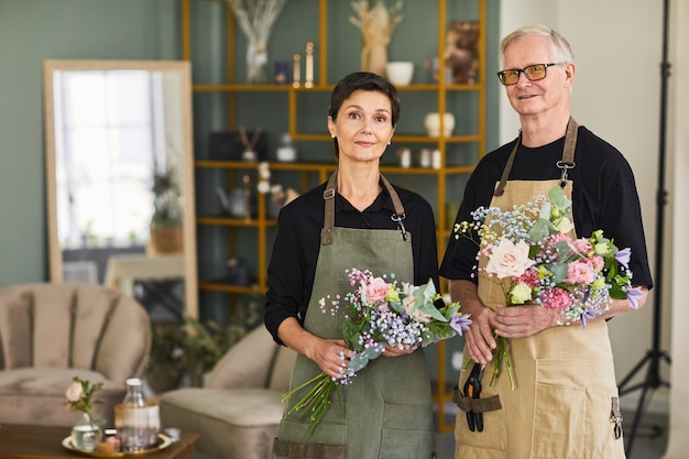 Cintura para arriba retrato de dos floristas maduros sosteniendo ramo mientras está de pie en la tienda de flores y mirando un ...