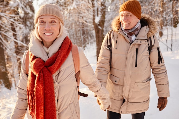 Cintura para arriba retrato de feliz pareja senior disfrutando de caminar en el bosque de invierno y tomados de la mano