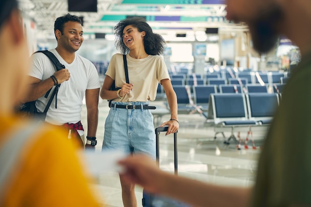 Cintura para arriba retrato de gente de carrera de caja de risa con equipaje caminando en el vestíbulo del aeropuerto