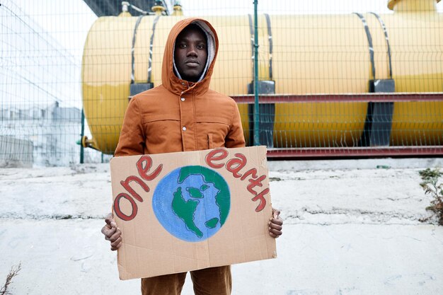 Cintura para arriba retrato de hombre afroamericano sosteniendo un signo de tierra y mirando a la cámara mientras protesta ...