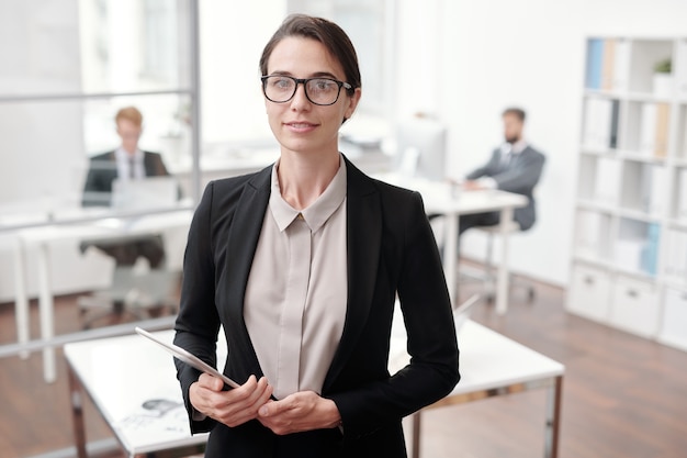 Cintura para arriba retrato de joven empresaria y sosteniendo tableta digital mientras está de pie en la oficina, espacio de copia