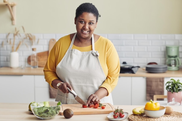 Cintura para arriba retrato de joven negra cocinando ensalada saludable en la cocina y cortando verduras copia