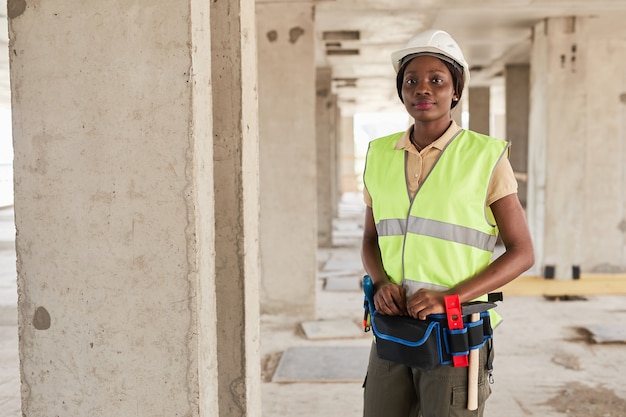 Cintura para arriba retrato de mujer afroamericana joven que trabaja en el sitio de construcción y sonriendo a la cámara ...