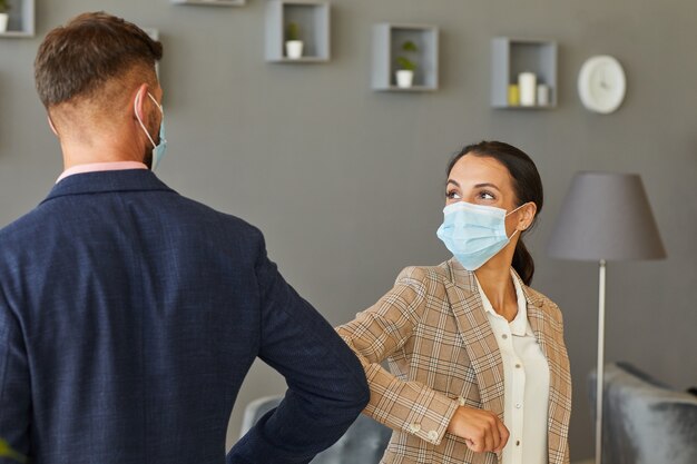 Cintura para arriba retrato de mujer de negocios moderna con máscaras y golpeando los codos como saludo sin contacto en la oficina posterior a la pandemia, espacio de copia