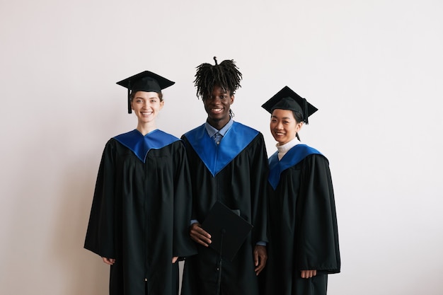 Cintura para arriba retrato de tres graduados universitarios vistiendo túnicas y sonriendo a la cámara, espacio de copia