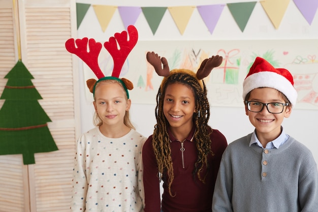 Cintura para arriba retrato de tres niños con gorro de Papá Noel y mirando a la cámara mientras disfruta de clase en Navidad, espacio de copia