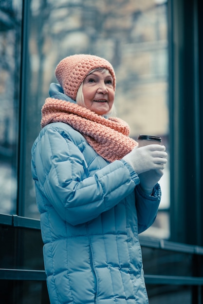 Cintura de um calmo aposentado caminhando ao ar livre em um dia de inverno e segurando uma xícara de café