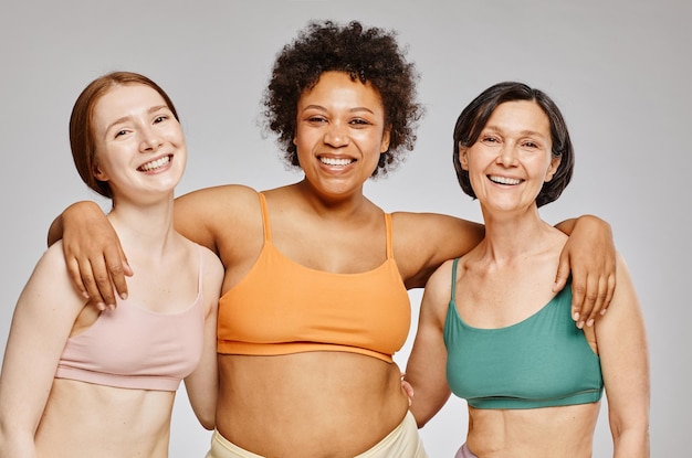 Foto cintura mínima para arriba grupo diverso de mujeres reales que usan ropa interior y se ríen alegremente contra el bac gris