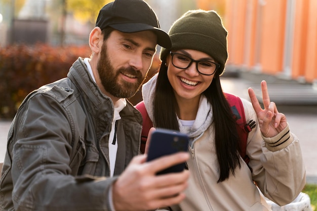 Cintura para cima retrato de jovem casal apaixonado feliz curtindo um encontro na rua enquanto abraça e faz selfie de felicidade no smartphone moderno