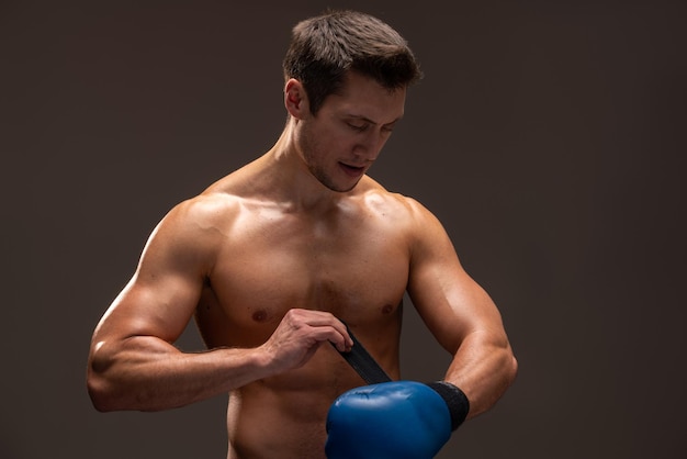 Cintura para cima retrato de um homem de fitness envolvendo suas luvas de boxe azuis isoladas em um fundo marrom. Conceito de esporte