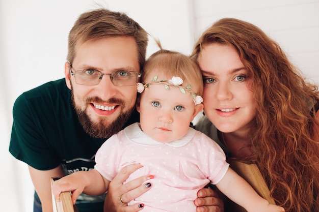 Cintura para cima sorrindo jovem pai e mãe abraçando seu bebê recém-nascido enquanto posavam para a câmera. conceito de paternidade