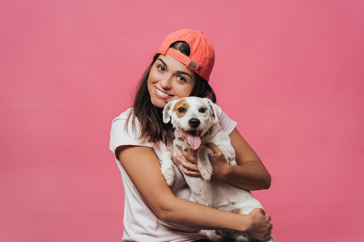 Foto cintura para cima tiro de caucasiano jovem fêmea detém firmemente filhote de cachorro, ri sinceramente, se alegra presente de amigo, gosta de animais dedicados