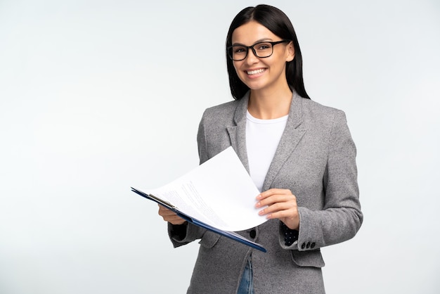 Cintura para cima, vista de retrato da encantadora empresária segurando uma pasta aberta e sorrindo para a câmera contra um fundo branco