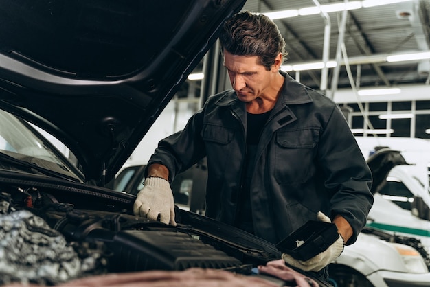 Cintura para cima vista de retrato do mecânico de automóveis sério em sua oficina ao lado do carro. Close do motor