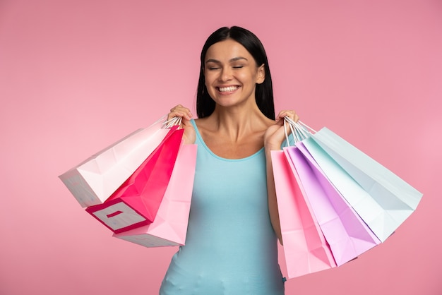 Cintura para cima, vista do tamanho do corpo dela, ela bonita, elegante, carregando mercadorias de coisas novas, isoladas em um fundo de cor rosa vibrante de brilho vívido brilhante