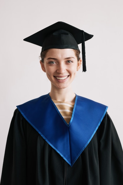 Cintura vertical para arriba retrato de mujer joven vistiendo batas de graduación y sonriendo a la cámara