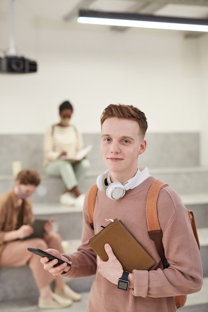 Cintura vertical para cima retrato de jovem estudante do sexo masculino sorrindo para a câmera em pé no moderno salão da escola