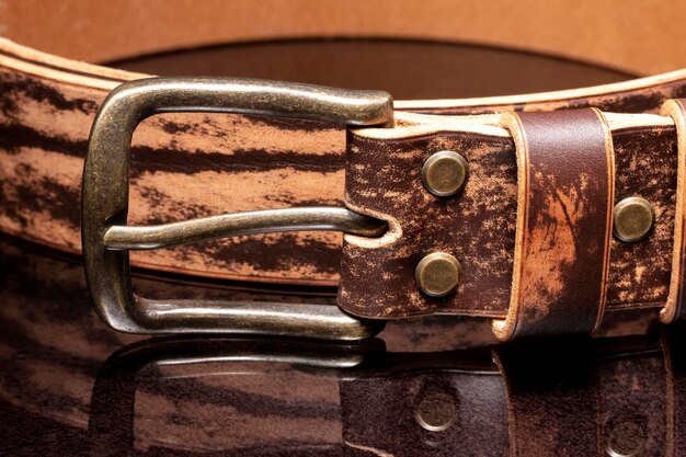 Cinturón de cuero marrón con rozaduras y hebilla de metal sobre un fondo oscuro.