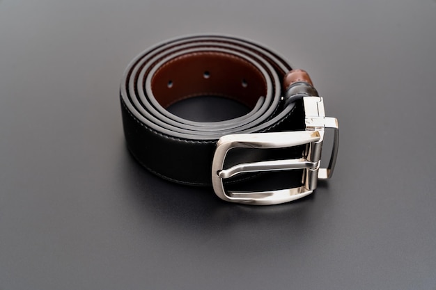 Cinturón de cuero negro y marrón de doble cara con hebilla desabrochada sobre fondo negro