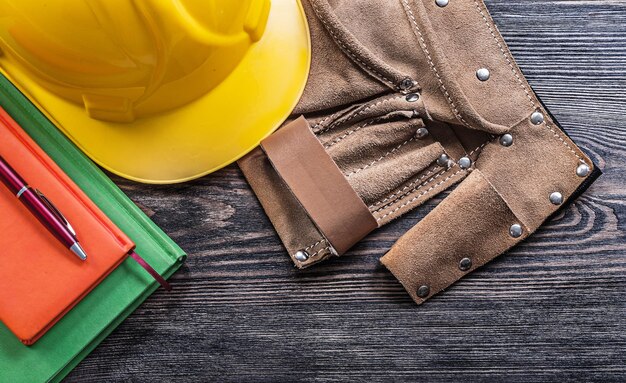 Cinturón de herramientas de cuero, blocs de notas, bolígrafo, casco de construcción protector en concepto de construcción de tablero de madera