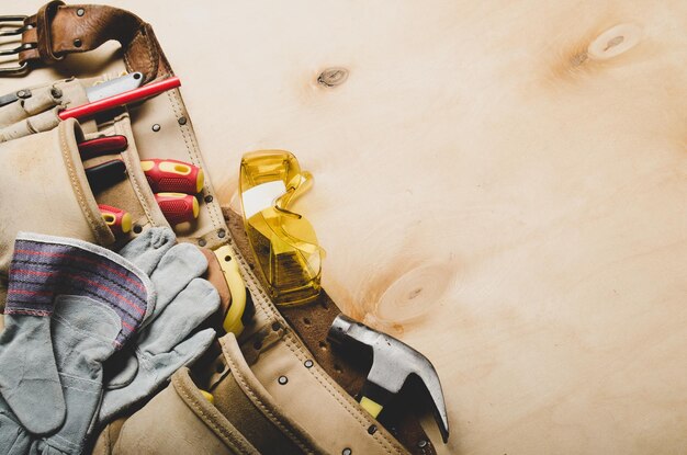 Cinturón de herramientas con herramientas de carpintero y ropa protectora en la vista plana de la hoja de madera contrachapada