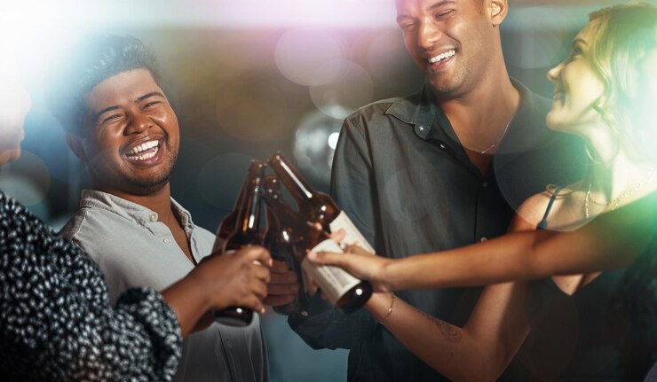 Foto círculo de cerveja ou brinde de pessoas em evento de boate de festa ou discoteca bokeh para comemoração de aniversário amigos bebidas ou reunião social sorriso feliz ou diversidade de união com garrafa de álcool em diversão