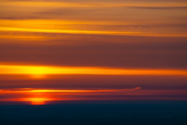 Círculo de sol vermelho grande nasce por trás do horizonte escuro em nuvens LANXESS de fundo de tons quentes.