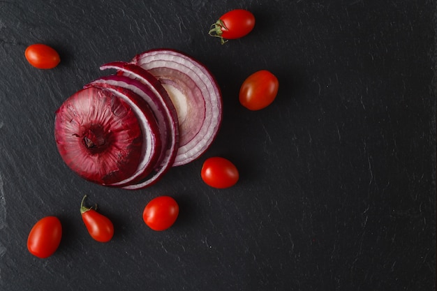 Círculos de cebolla roja con tomates en pizarra