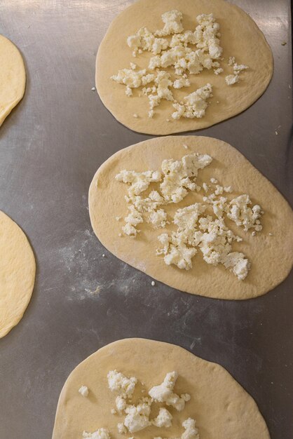 Círculos de massa recheados com queijo para bolinhos e tortas estão em uma placa de metal Massa crua e alimentos Preparação para assar produtos de pão