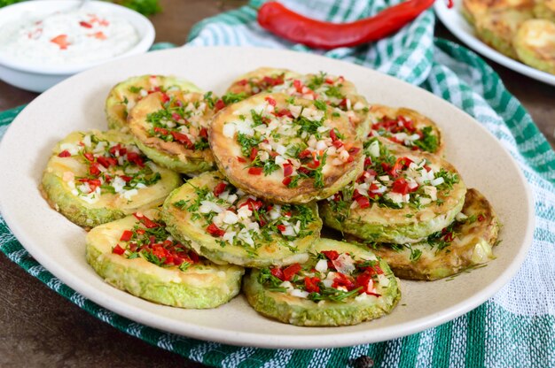 Círculos fritos de abobrinha jovem com alho, pimenta, verdes em um prato. Menu vegetariano.