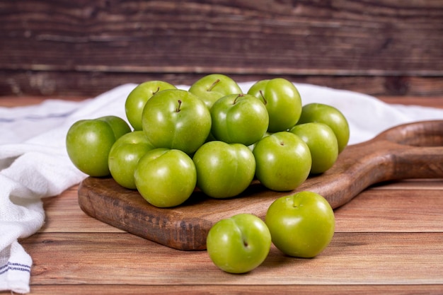 Ciruela verde sobre fondo de madera Montón de ciruelas verdes sobre un plato de madera para servir de cerca