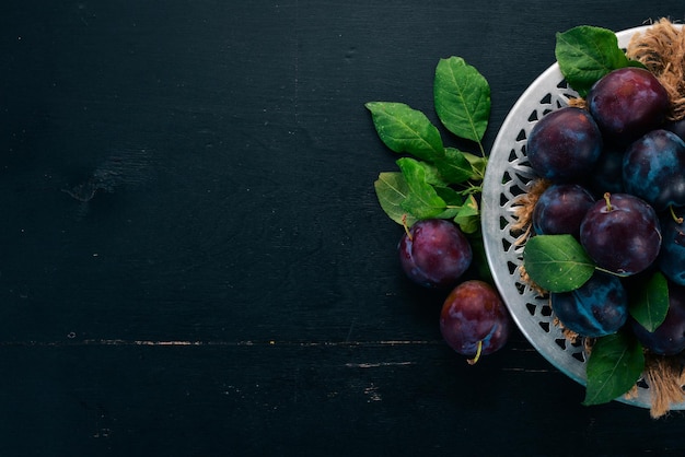 Ciruelas frescas con hojas Frutas Sobre un fondo de madera negra Vista superior Espacio libre para el texto