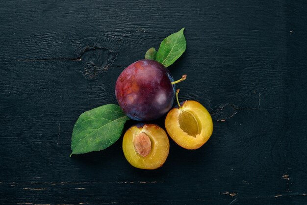 Ciruelas frescas con hojas Frutas Sobre un fondo de madera negra Vista superior Espacio libre para el texto