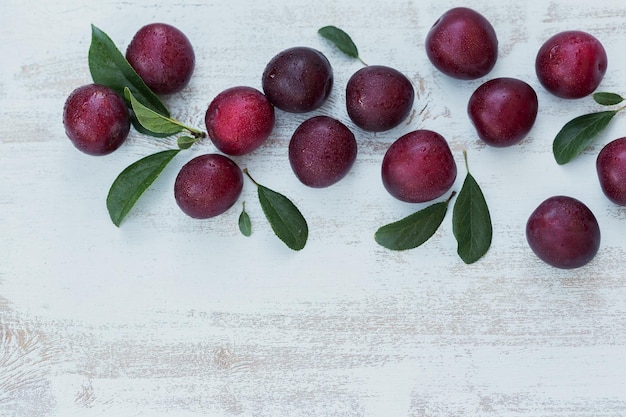 Ciruelas frescas con hojas sobre fondo de mesa de madera rústica blanca