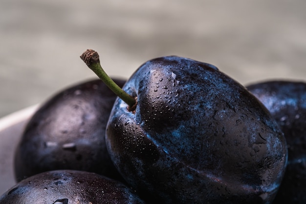 Ciruelas maduras frescas con gotas de agua sobre fondo de hormigón de piedra, vista de ángulo macro