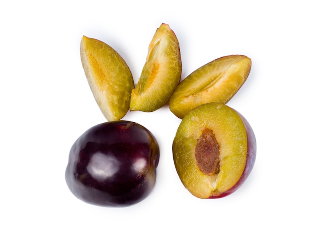 Ciruelas púrpuras frescas enteras, cortadas a la mitad y en rodajas para un postre saludable sobre un fondo blanco, vista aérea